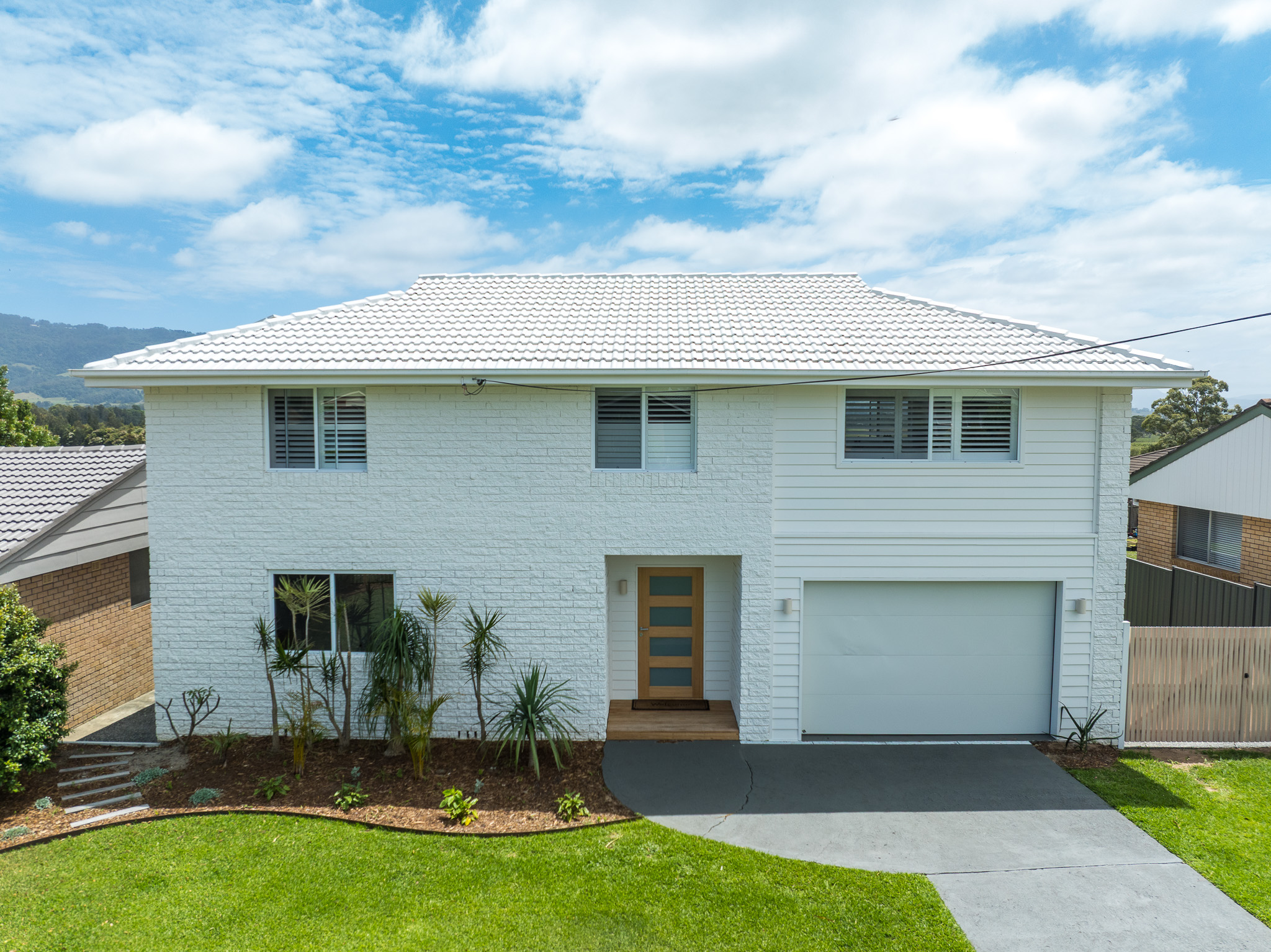 Exterior view of a modern two-story custom home in Bomaderry, built by Porter Building Group, featuring white painted brickwork, horizontal weatherboard cladding, and a natural timber front door.